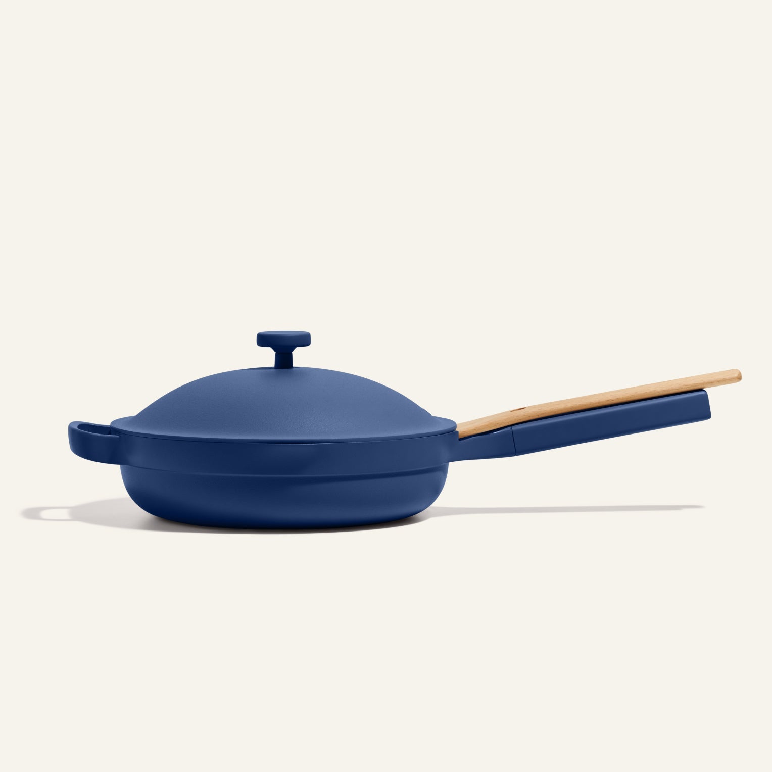 The Always Pan 2.0, a blue nonstick frying pan with a matching lid and long wooden handle from a bestselling cookware set, is displayed against a simple light background.