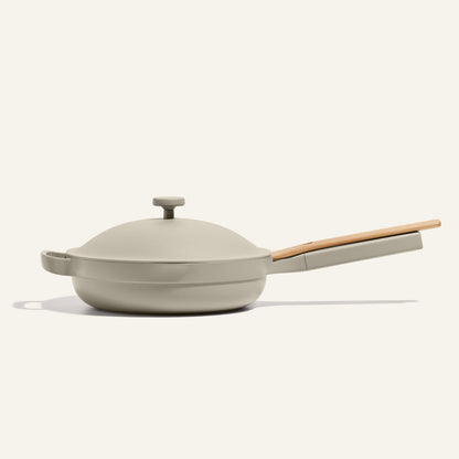 The Always Pan 2.0 is a beige nonstick frying pan with a matching lid and light wooden handle, from a bestselling cookware line, displayed on a plain light background.