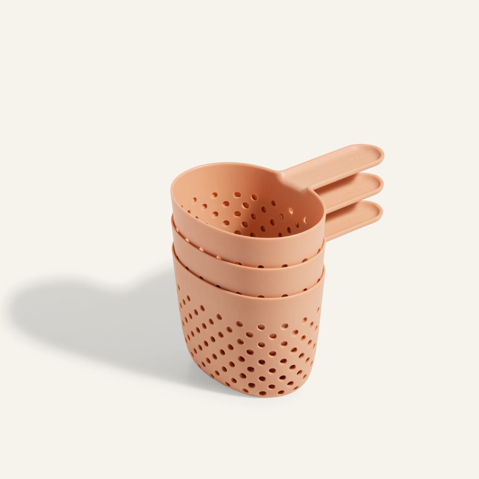 The Cooker Cups are three stackable, peach-colored plastic colanders with handles and evenly spaced holes—perfect for straining and multi-cooking when using your Perfect Pot.