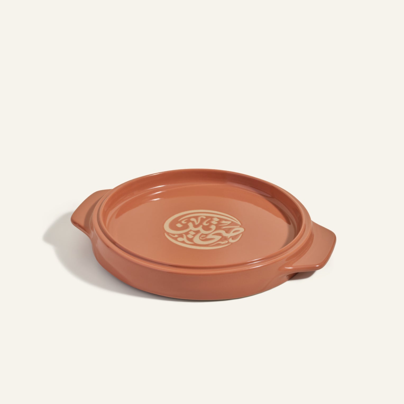 The Flipping Platter is a round terracotta baking dish with two side handles and a beige pattern in the center, ideal for serving maqluba or tahdig, shown against an off-white background.