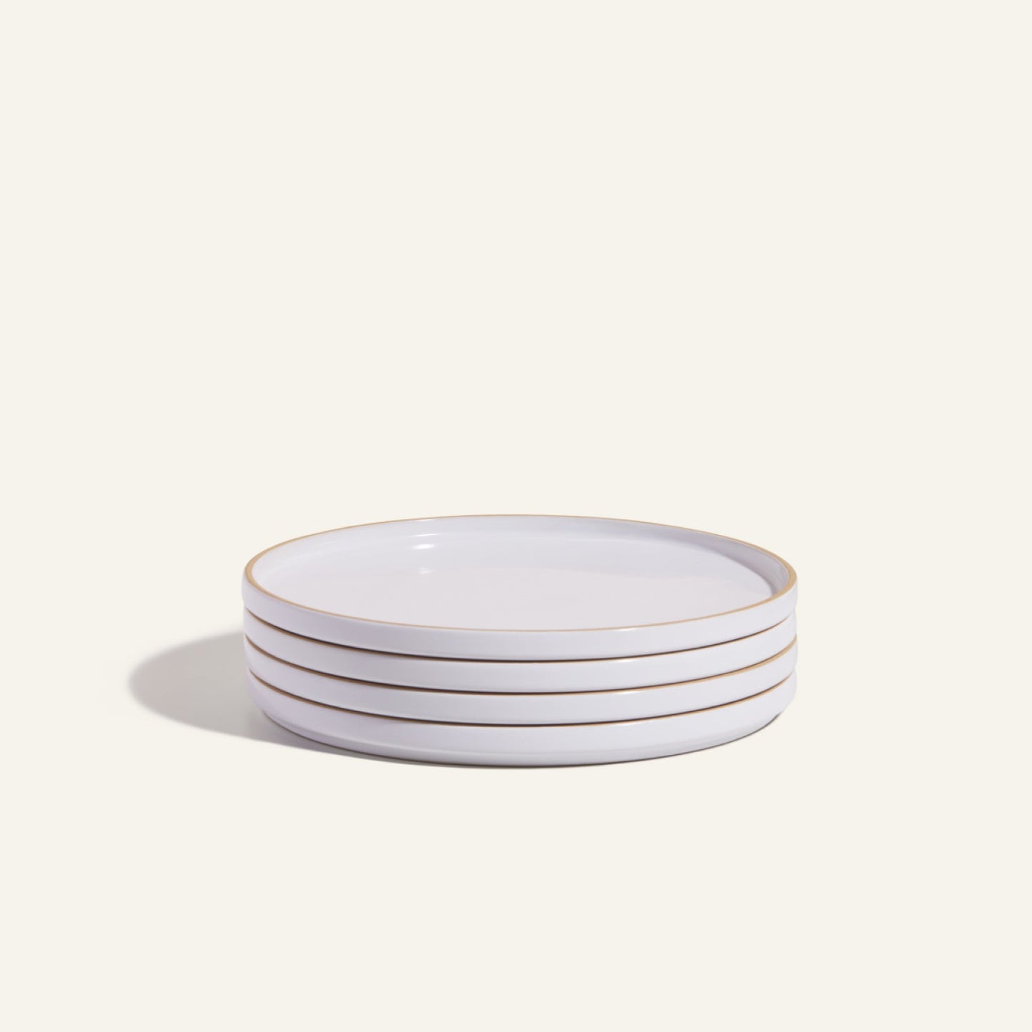A set of four white hand-glazed ceramic Dinner Plates, each featuring a thin gold rim, stacked elegantly against a simple light background.
