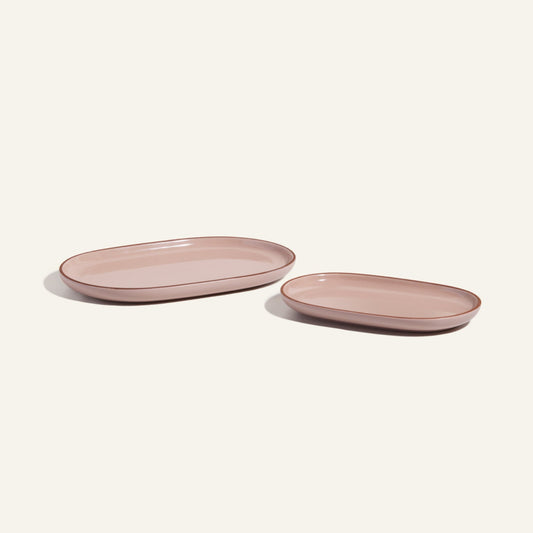 Two Serving Platters in pink oval ceramic, each a different size, are arranged side by side on a light background to highlight their elegant stackable design.