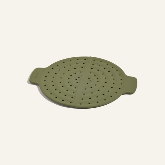 The Fearless Fry is a round, green silicone steamer lid with dual handles and evenly spaced holes to prevent splatter—perfect for use with your Always Pan.