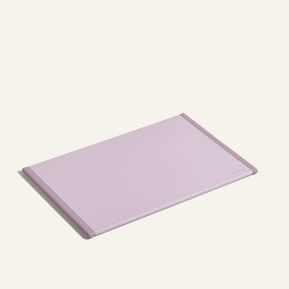 The Daily Board, a rectangular, light purple cutting board crafted from recycled materials with beveled edges, is displayed on a plain, light background.