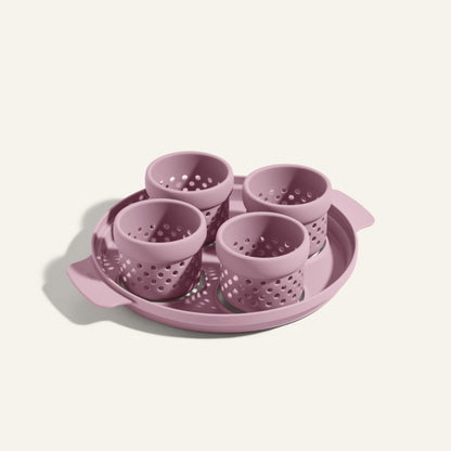 The Egg Poacher includes four pink silicone cups for poaching eggs, all arranged on a matching round plastic tray with handles.