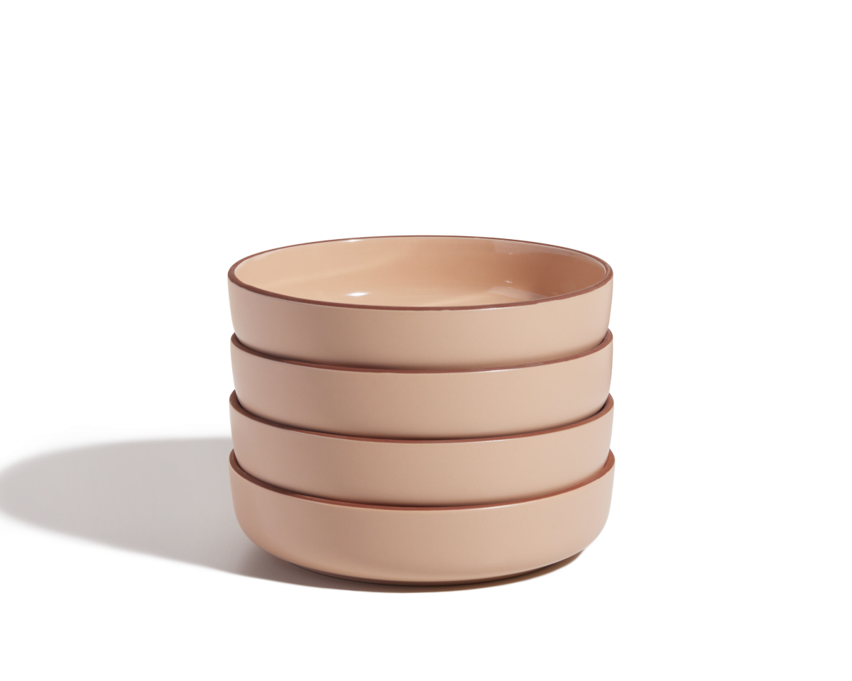 A stack of four beige scratch-resistant Dinner Bowls with brown rims sits on a white surface, casting a shadow to the left.
