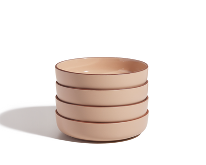 A stack of four beige scratch-resistant Dinner Bowls with brown rims sits on a white surface, casting a shadow to the left.