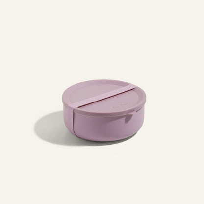 The Wander Bowl is a round, light purple ceramic bowl with a matching lid that’s microwave safe—shown on a plain off-white background.