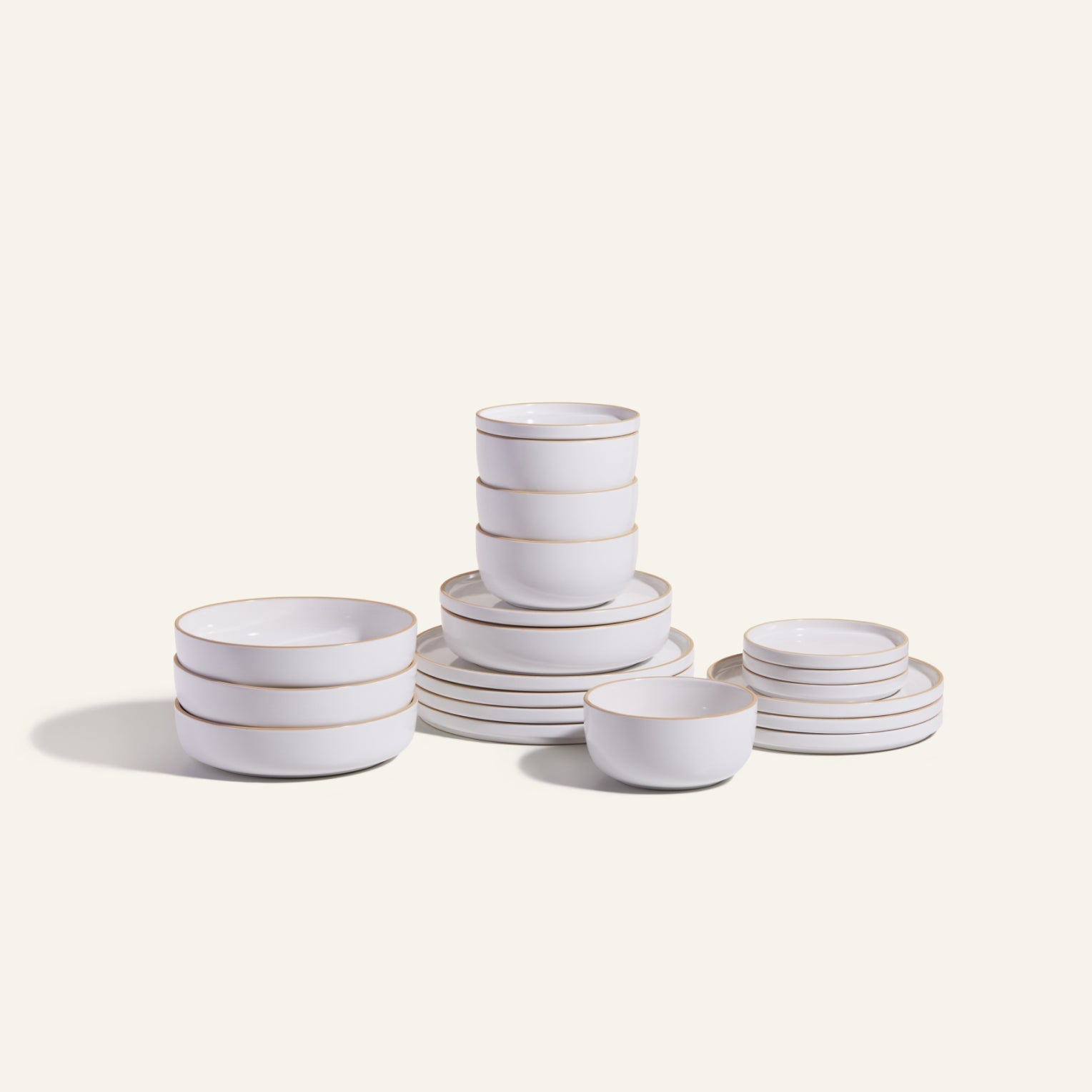 The Classic Stacking Set is a 20-piece ceramic tableware collection with matching white bowls and plates, each adorned with thin gold rims, attractively stacked against a plain light background.
