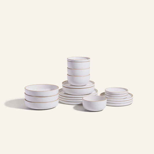 The Classic Stacking Set is a 20-piece ceramic tableware collection with matching white bowls and plates, each adorned with thin gold rims, attractively stacked against a plain light background.