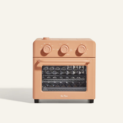 The AU - Wonder Oven is a compact, rectangular peach toaster oven with three control dials and a clear window revealing two metal racks. Ideal for countertops, it also functions as a versatile air fryer.