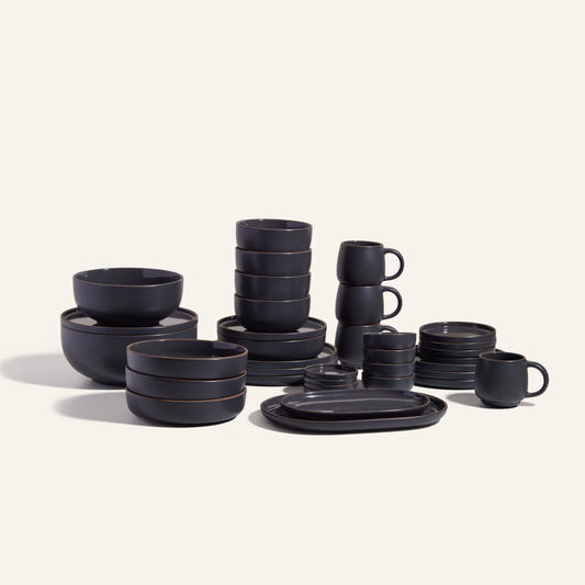 The Complete Stacking Set features matte black ceramic bowls, plates, and mugs arranged on a light background—an ideal, stylish hosting set for any occasion.