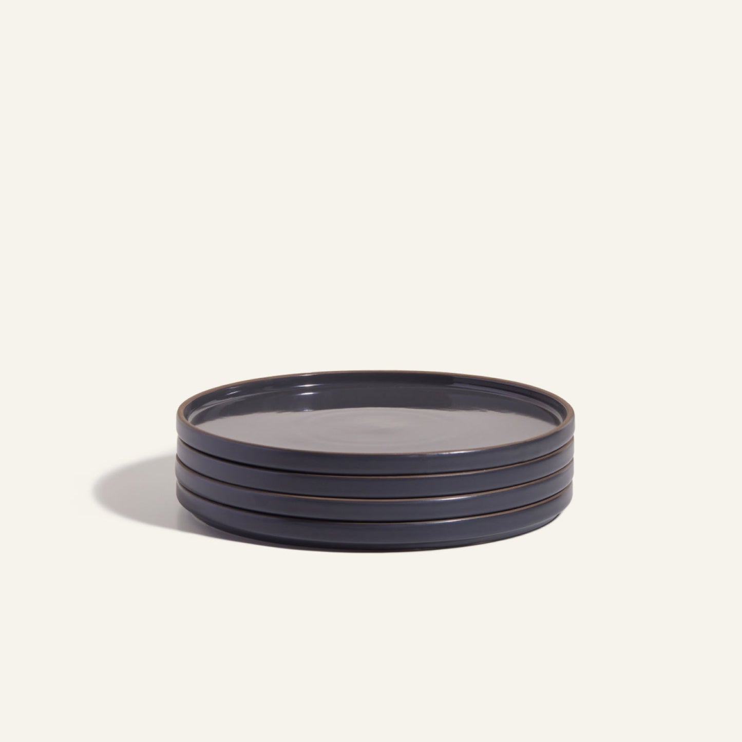A stack of four round, dark-colored Dinner Plates with a hand-glazed finish rests on a plain light background, highlighting elegant ceramic tableware.