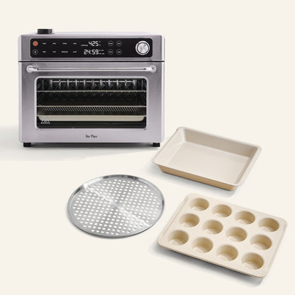The Wonder Oven Pro + Wonder Oven Pro Chef's Kit, a stainless steel countertop oven with digital controls, is shown with a muffin tin, square baking pan, and round perforated tray on a light background.