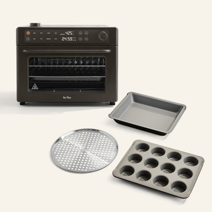 The Wonder Oven Pro + Wonder Oven Pro Chef's Kit, featuring a black digital countertop oven, a baking tray, perforated round tray, and twelve-cup muffin pan, is displayed on a light background.