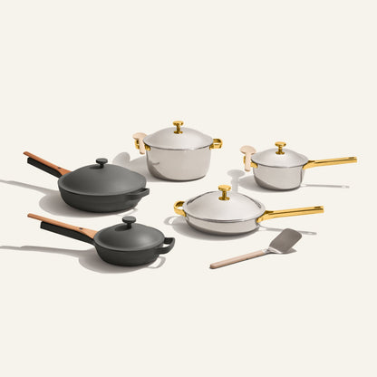 The Home Chef Set (15 piece) includes two black pans, three white ceramic pots with gold handles, and a metal spatula, all displayed on a light background.