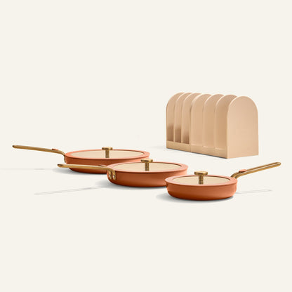 Set of three frying pans with lids and a beige stand on a white background