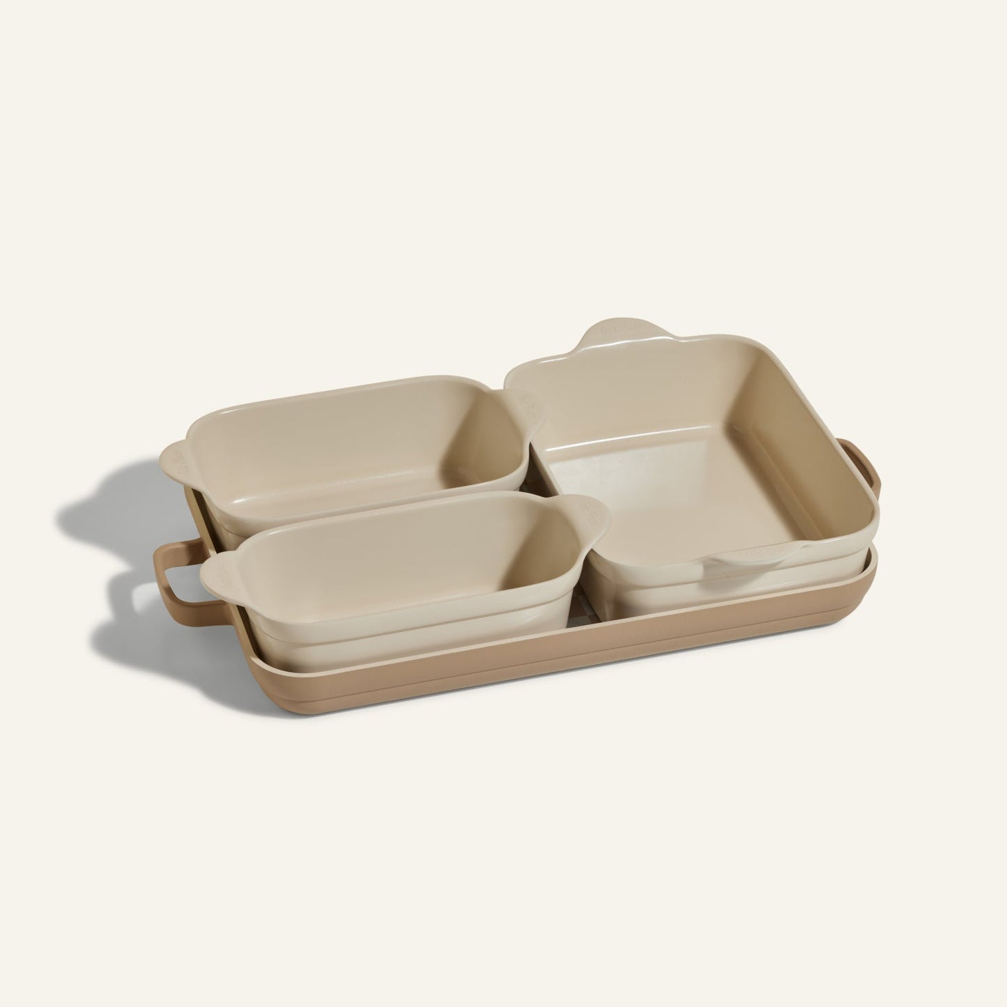 The Bakeware Set includes four beige ceramic baking dishes stacked on a large rectangular tray, making it an essential and versatile addition to any kitchen.